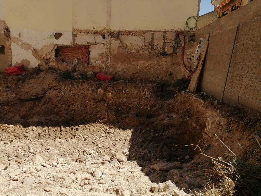 Gran área de tierra removida en una obra de construcción con un primer plano de grava y un muro al fondo.
