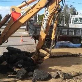 Una excavadora amarilla levanta escombros negros en una obra de construcción embarrada.