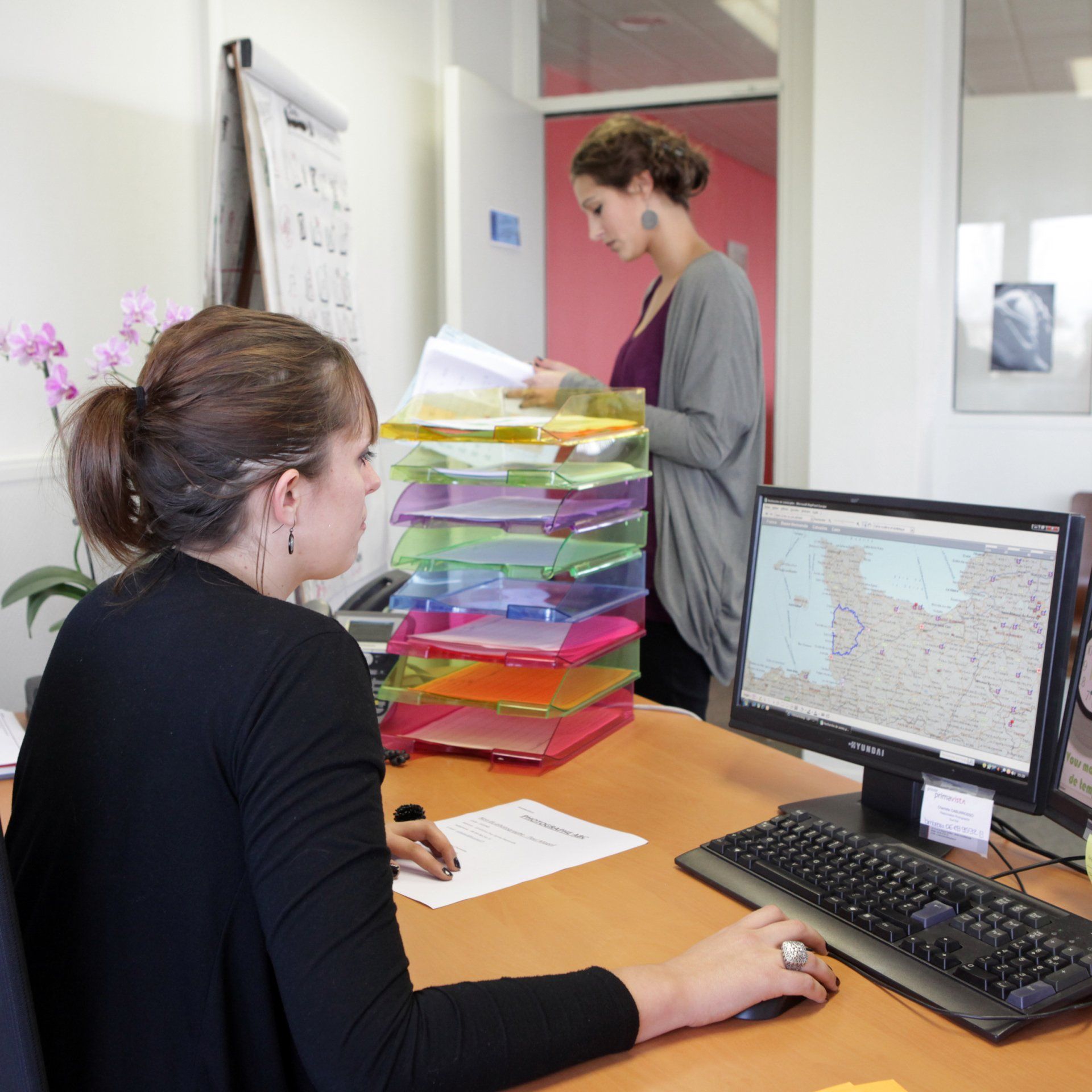 Femme derrière un ordinateur avec une autre qui lit des documents devant elle