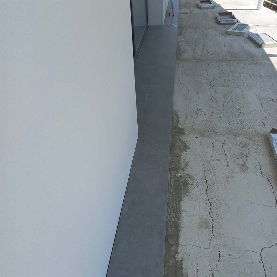 Una pasarela de hormigón gris junto a una pared blanca. El suelo es irregular y agrietado.