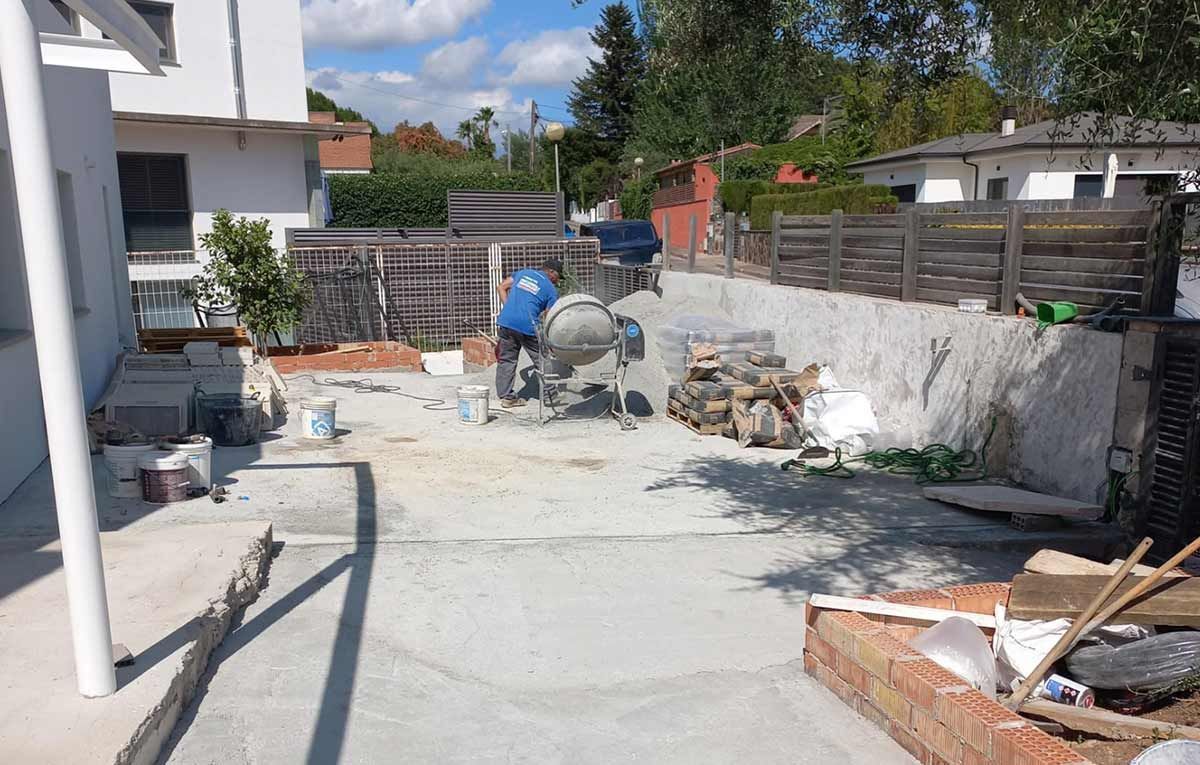 Obra: hormigonera, muro de ladrillos en proceso, suministros y edificación.