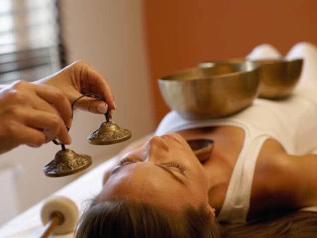 Des mains tenant de petits bols chantants près d’une personne allongée pendant une séance de sonothérapie au spa