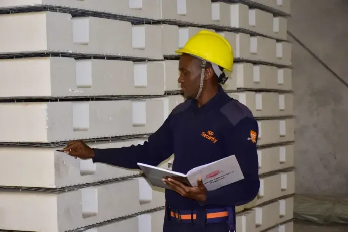 A man wearing a yellow hard hat is standing in front of a stack of boxes.