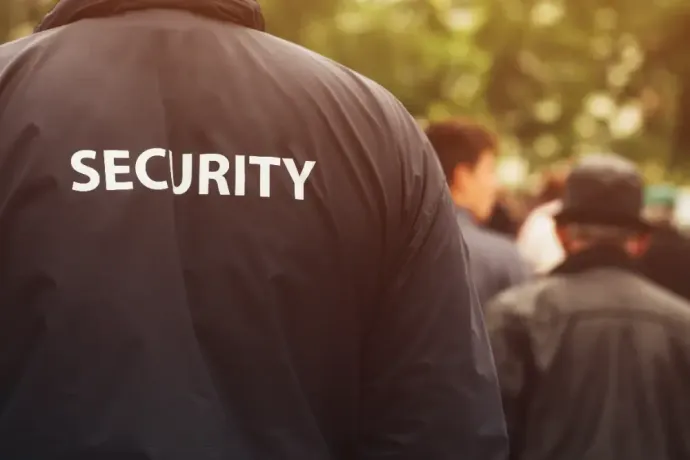 A security guard is standing in front of a crowd of people.