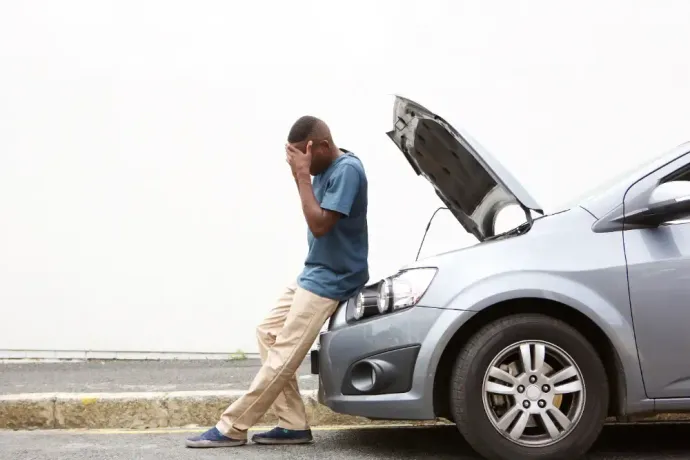 A man is standing next to a broken down car with the hood up.