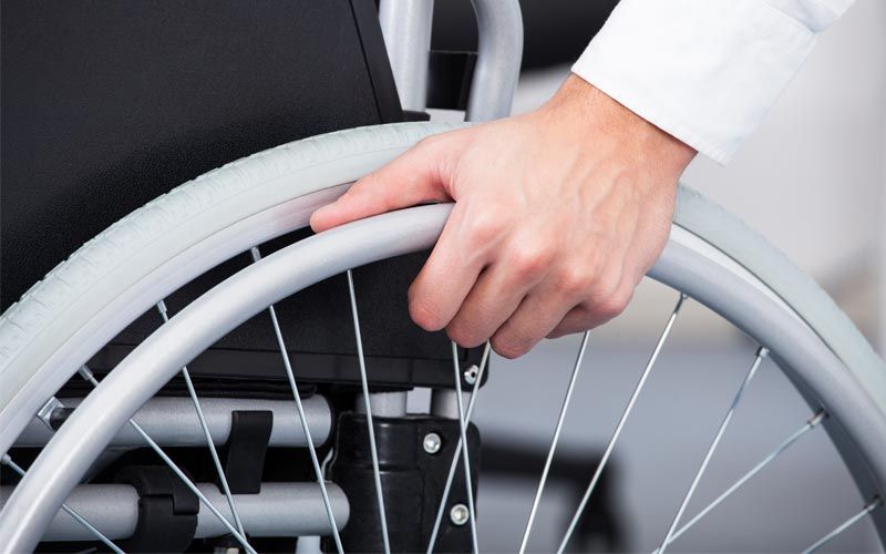 Gros plan d'une main tenant une roue de fauteuil roulant.