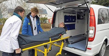 Deux secouristes chargent un patient sur une civière dans une ambulance blanche.