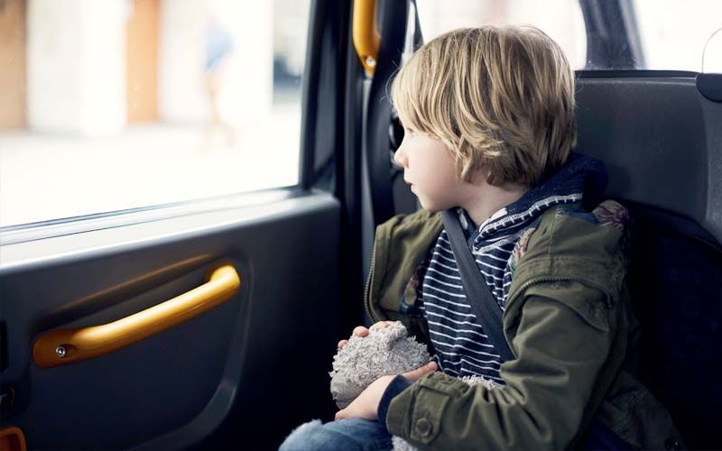 Garçon dans un taxi, regardant par la fenêtre, portant une veste et une ceinture de sécurité, tenant une peluche.