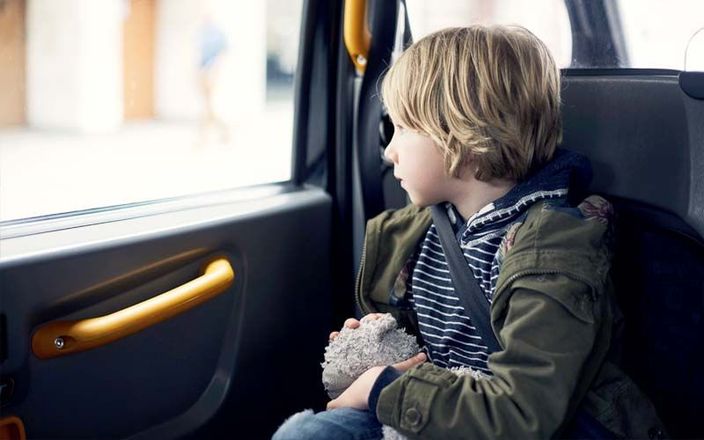 Un jeune enfant installé dans un siège auto regarde par la fenêtre, tenant un jouet.