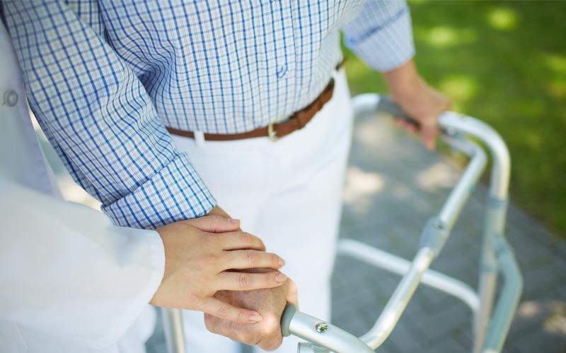 Personne utilisant un déambulateur assistée par une autre personne, à l'extérieur.