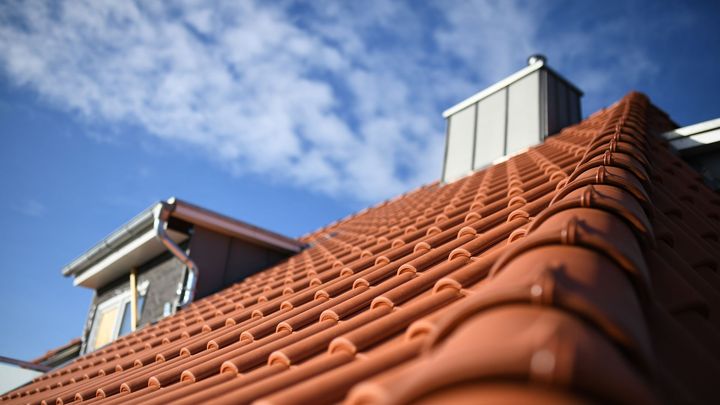Toit de tuiles rouges sur un bâtiment avec une cheminée, se détachant sur un ciel bleu nuageux.