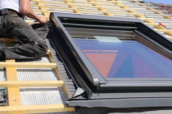 Couvreur installant une fenêtre de toit sur une toiture en construction. Poutres en bois et personne en tenue de travail.