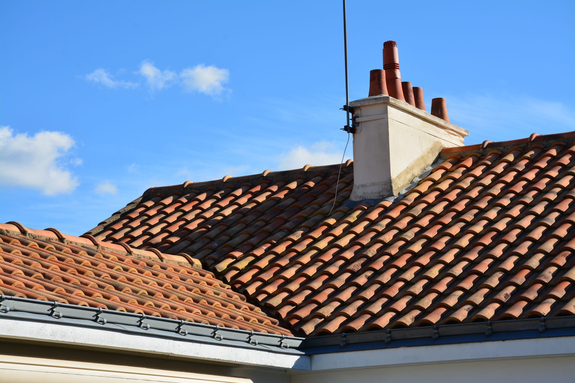 Toit de tuiles rouges avec cheminée et ciel bleu.