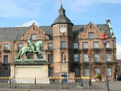 Ein großes Backsteingebäude mit einem Uhrenturm und einer Statue eines Mannes auf einem Pferd davor.