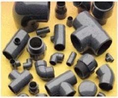 Un montón de accesorios de tubería de PVC están colocados uno encima del otro sobre una superficie amarilla.