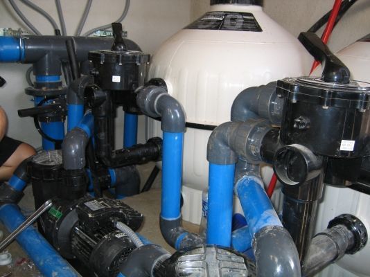 Un hombre está trabajando en una piscina con muchas tuberías.