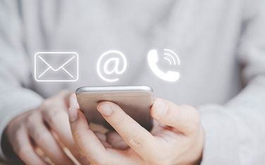 Una persona sostiene un teléfono celular del cual salen íconos de contacto.