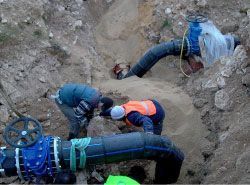 Dos hombres están trabajando en una tubería de agua en el suelo.