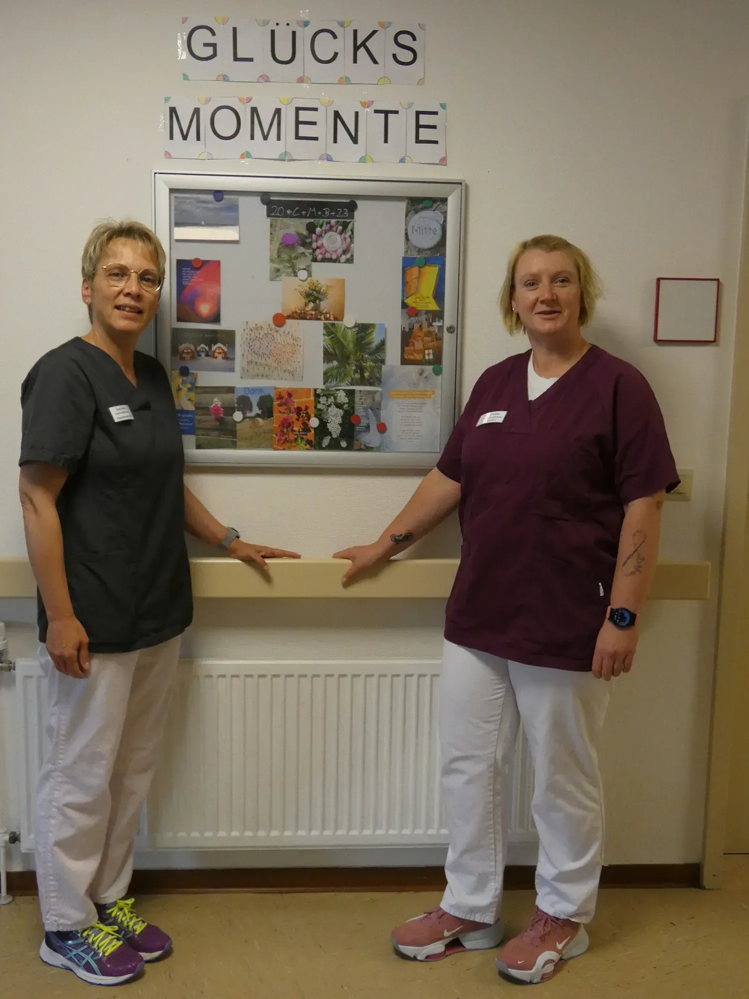 Zwei Frauen stehen vor einem Schild mit der Aufschrift „Glücksmomente“