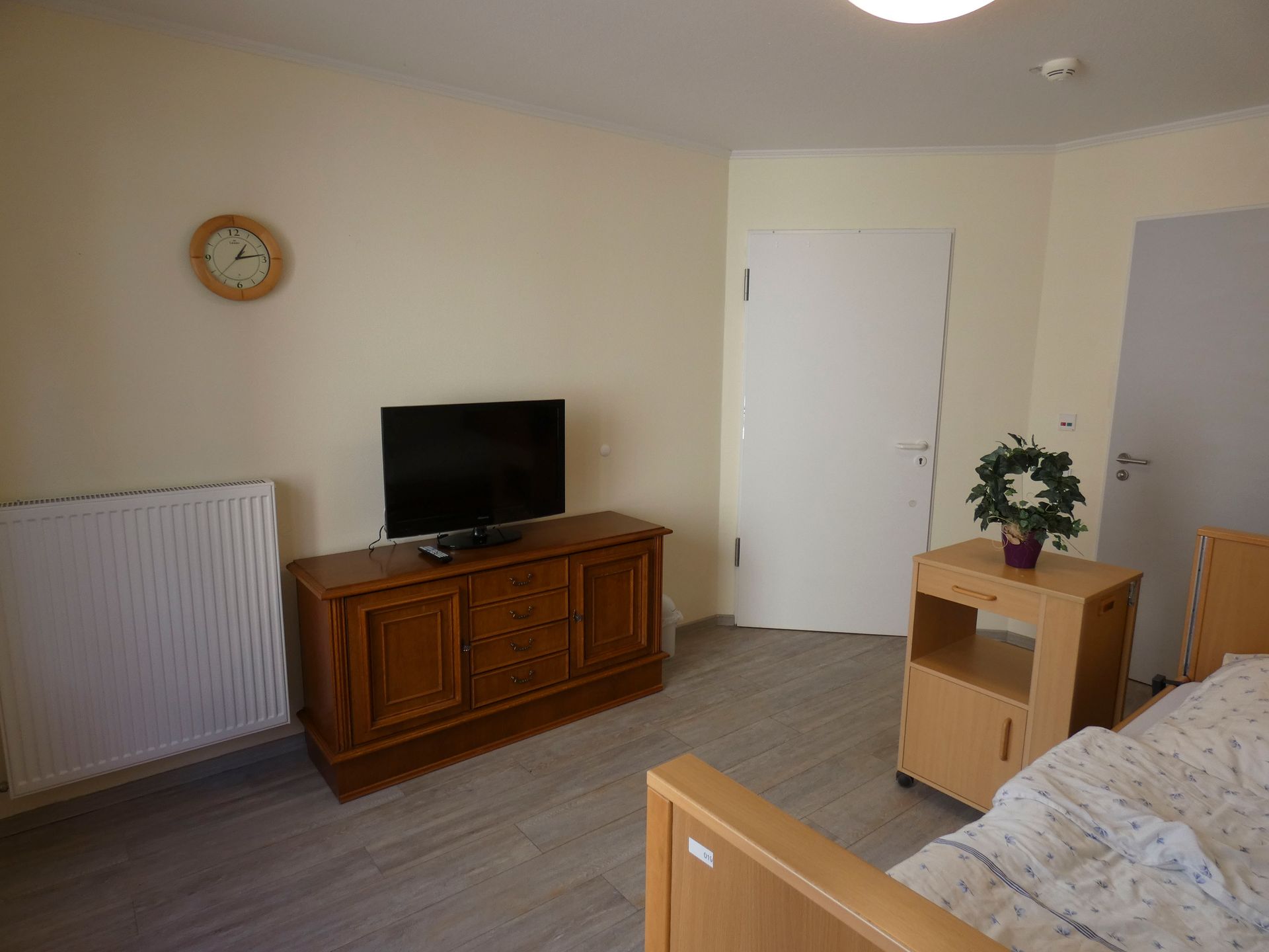 Ein Schlafzimmer mit Bett, Kommode, Fernseher und Uhr.