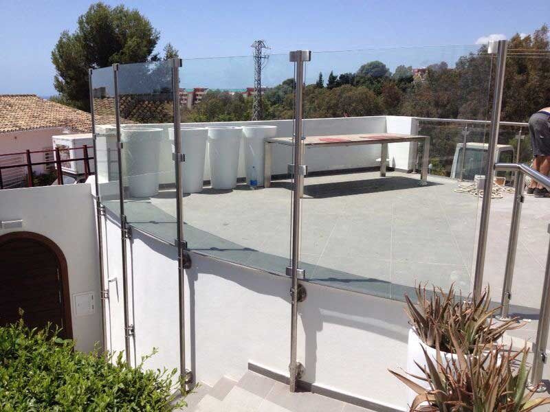 Un balcón con barandilla de cristal y una mesa encima.