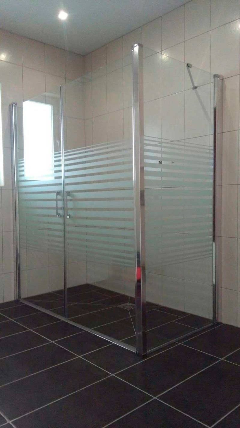 Un baño con ducha a ras de suelo y puerta de cristal rayado.