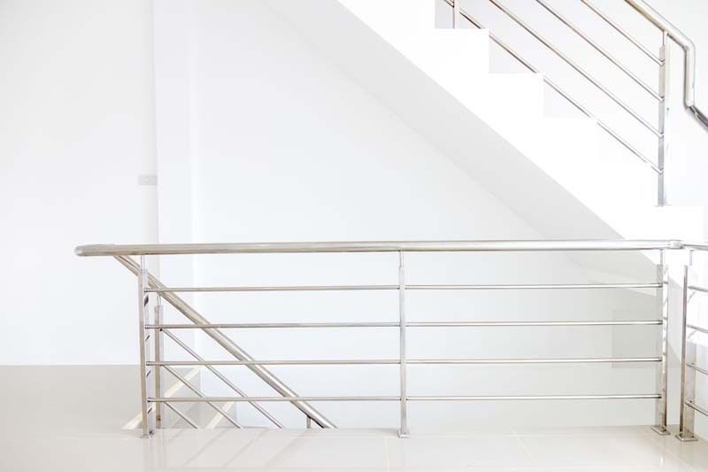 Una escalera vacía con barandilla de acero inoxidable y una pared blanca.