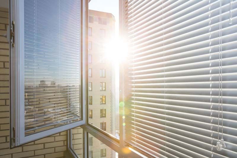 El sol brilla a través de las persianas de una ventana abierta.
