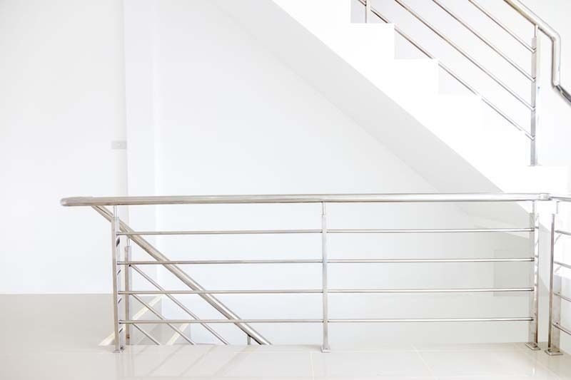 Una escalera vacía con barandilla de acero inoxidable y una pared blanca.