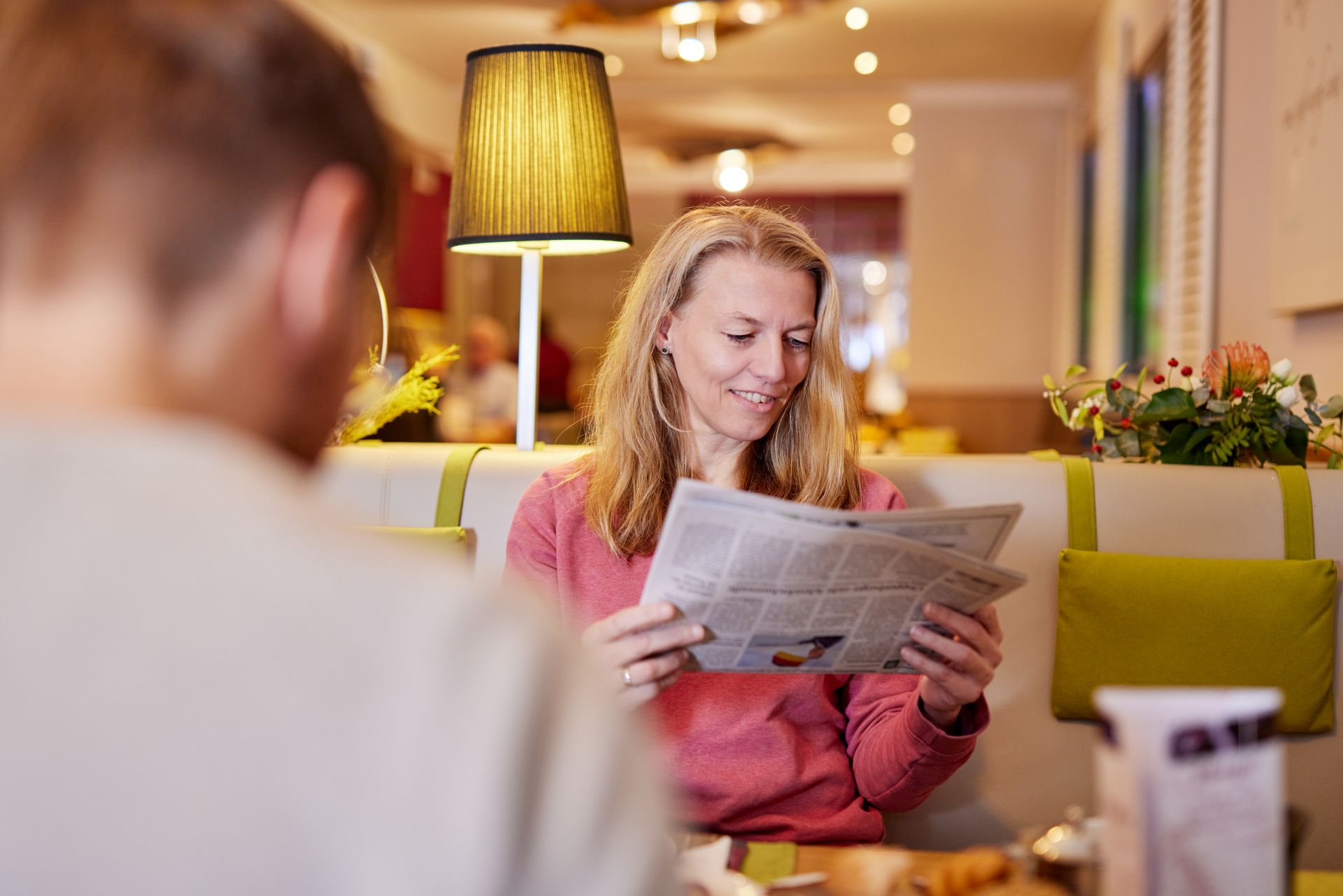 Eine Frau sitzt an einem Tisch und liest eine Zeitung.