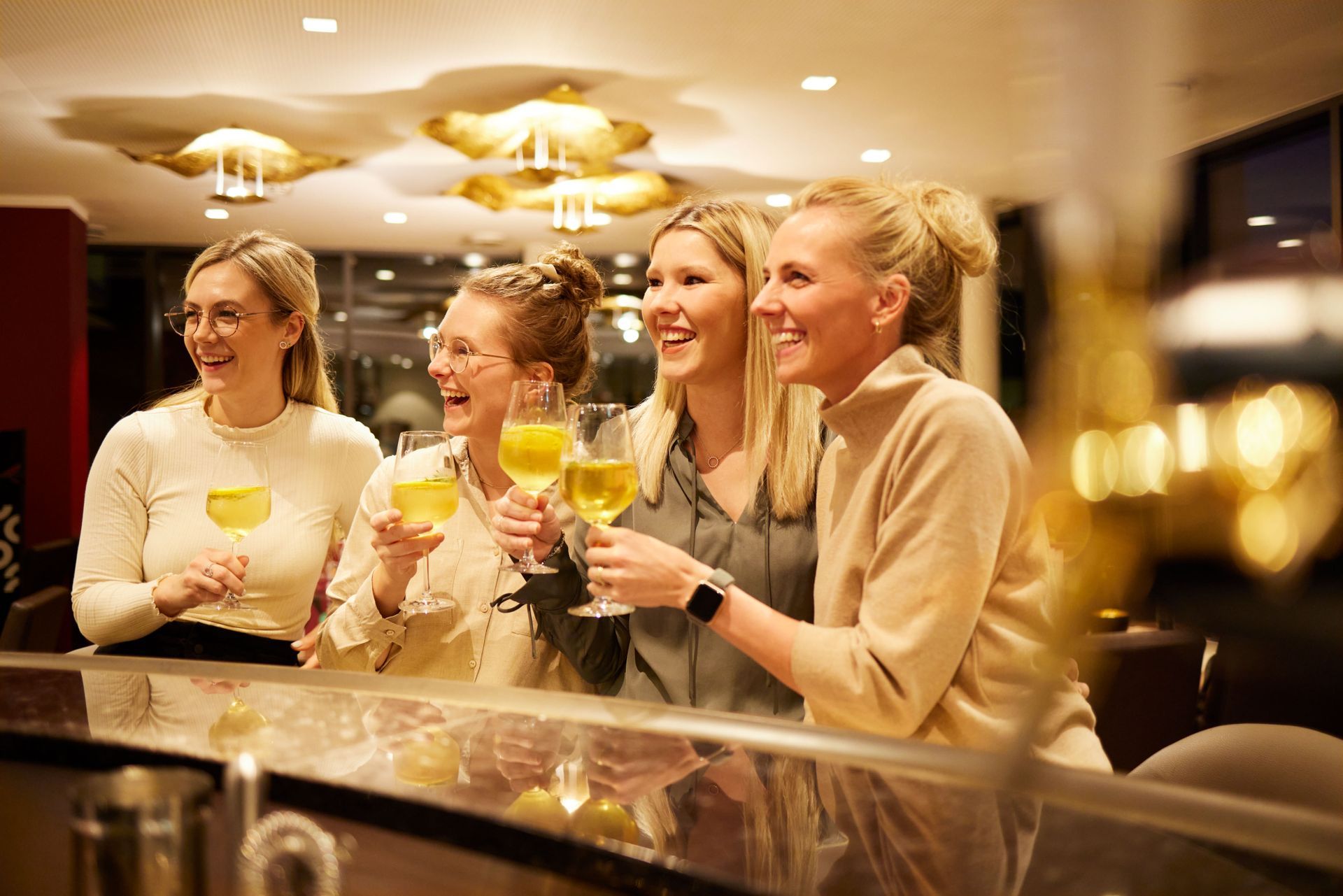 Eine Gruppe Frauen sitzt mit Weingläsern in der Hand an einer Bar.
