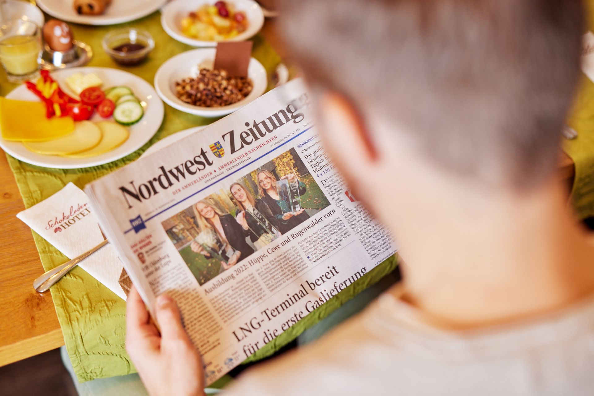 Eine Person sitzt an einem Tisch und liest eine Zeitung.