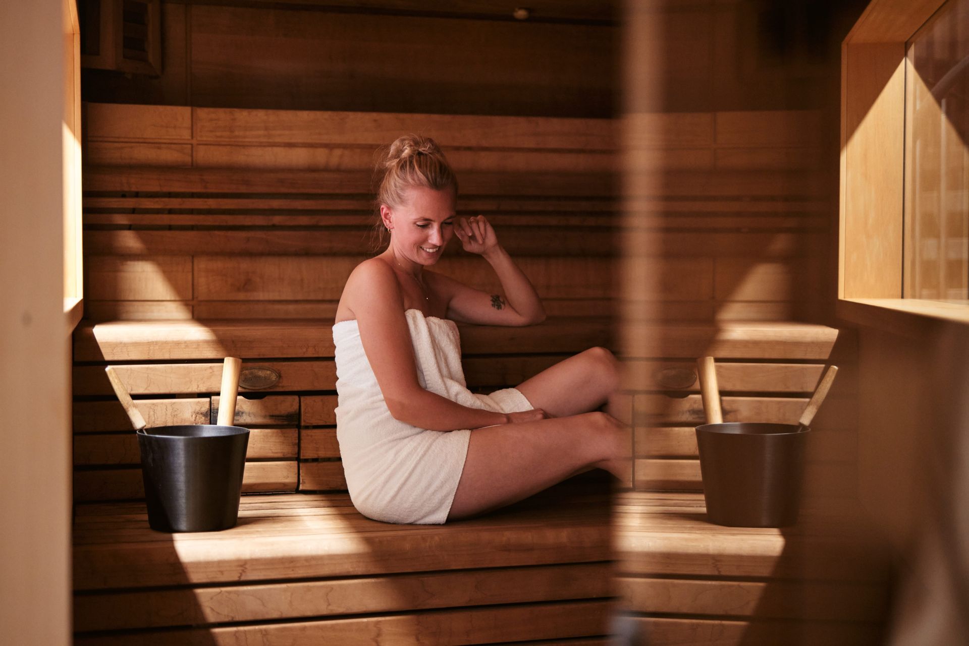 Eine in ein Handtuch gehüllte Frau sitzt in einer Holzsauna.