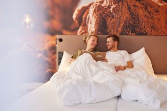 Ein Mann und eine Frau liegen im Bett und schauen auf ein Heft.