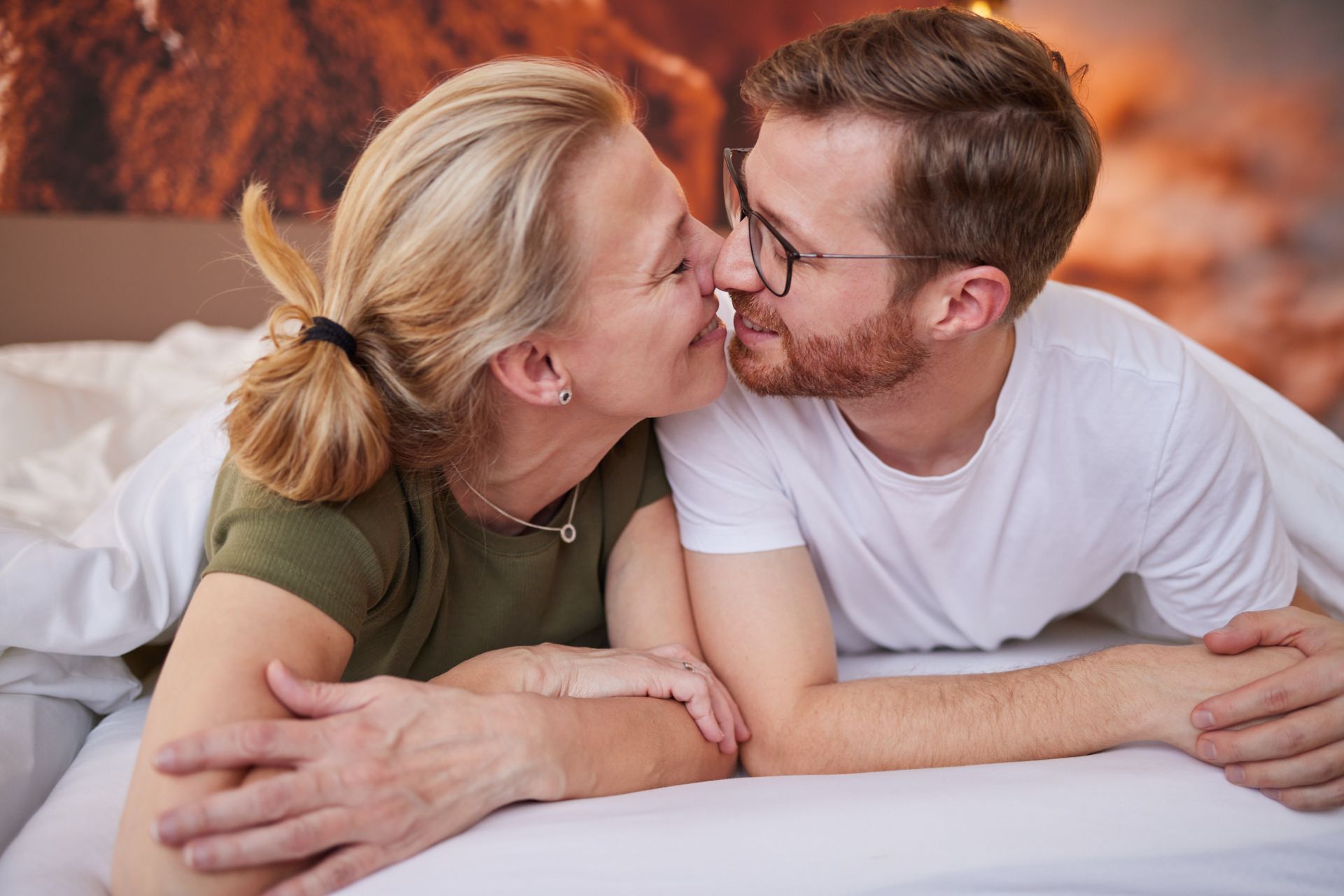 Eine Frau und ein Mann liegen nebeneinander im Bett und lächeln sich an.