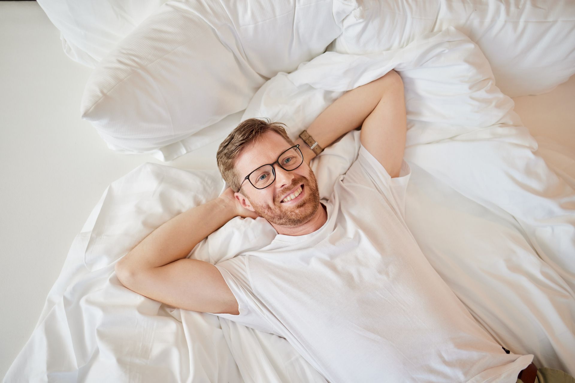 Ein Mann mit Brille liegt mit den Händen hinter dem Kopf auf einem Bett.