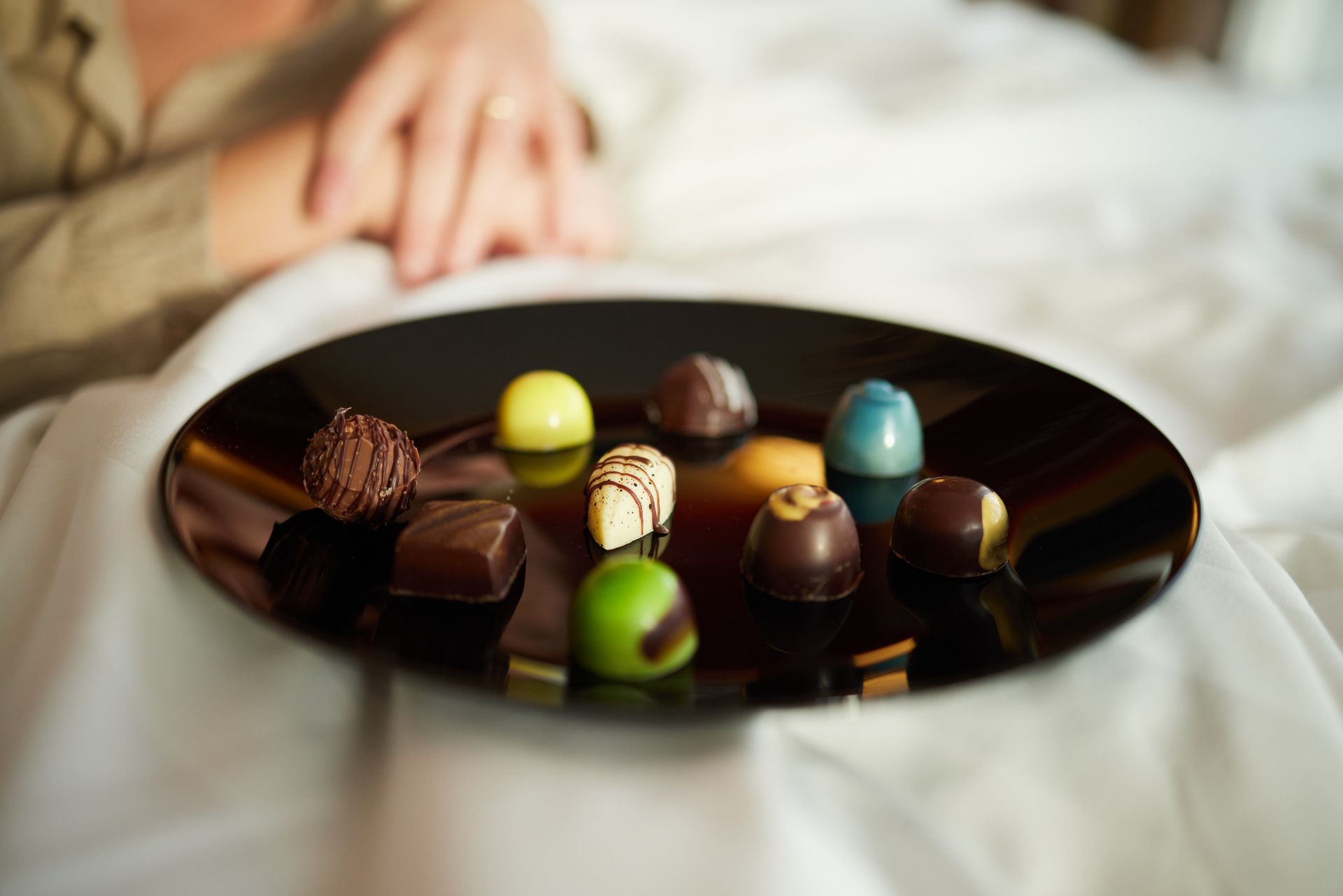 Eine Person hält einen Teller mit Pralinen auf einem Bett.