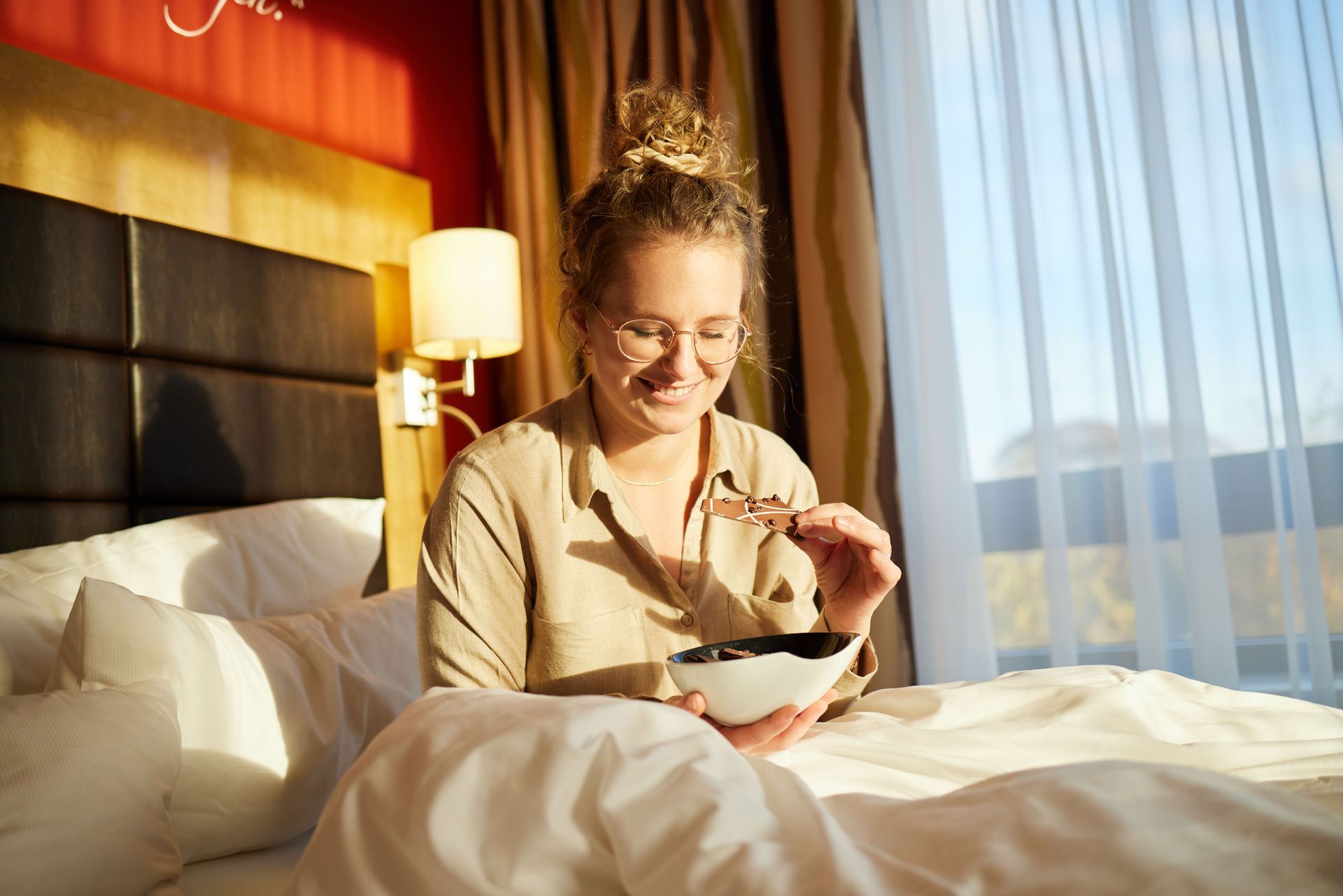 Eine Frau sitzt auf einem Bett und isst Schokolade.