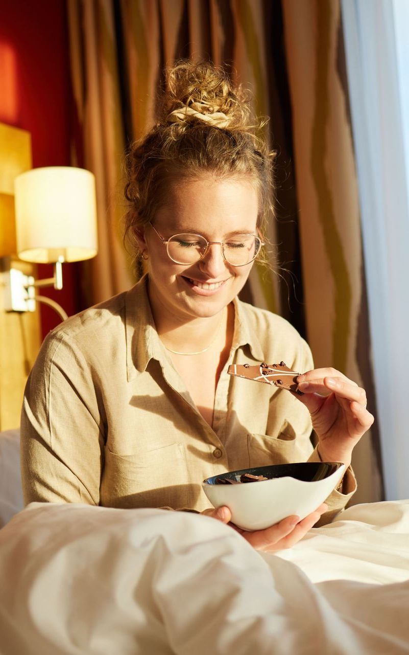 Eine Frau sitzt auf einem Bett und genießt ein Stück Schokolade.