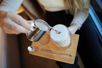 Eine Frau gießt Milch in eine Tasse Kaffee.