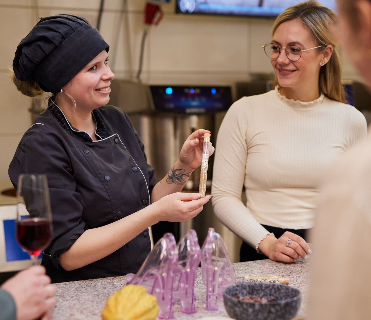 Eine Frau mit Kochmütze sitzt mit zwei anderen Frauen an einem Tisch.