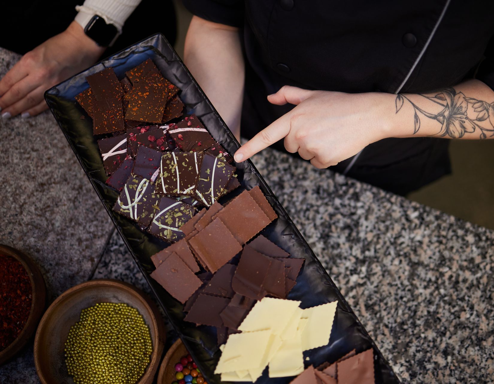 Eine Person zeigt auf ein Tablett mit verschiedenen Schokoladensorten