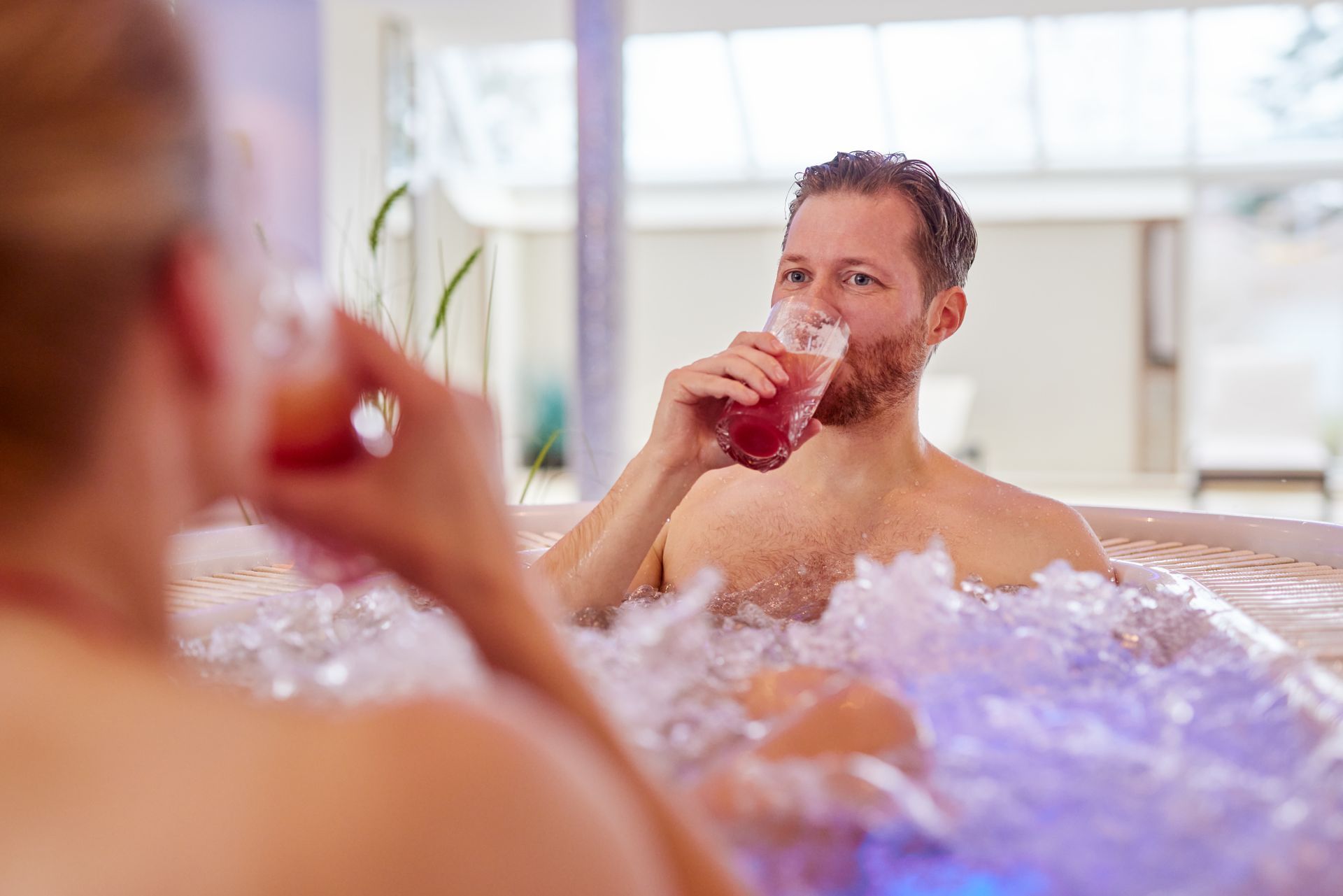 Ein Mann und eine Frau sitzen in einem Whirlpool und trinken Wein.