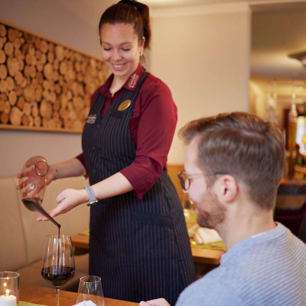 Eine Frau gießt Wein in ein Glas, während ein Mann an einem Tisch sitzt
