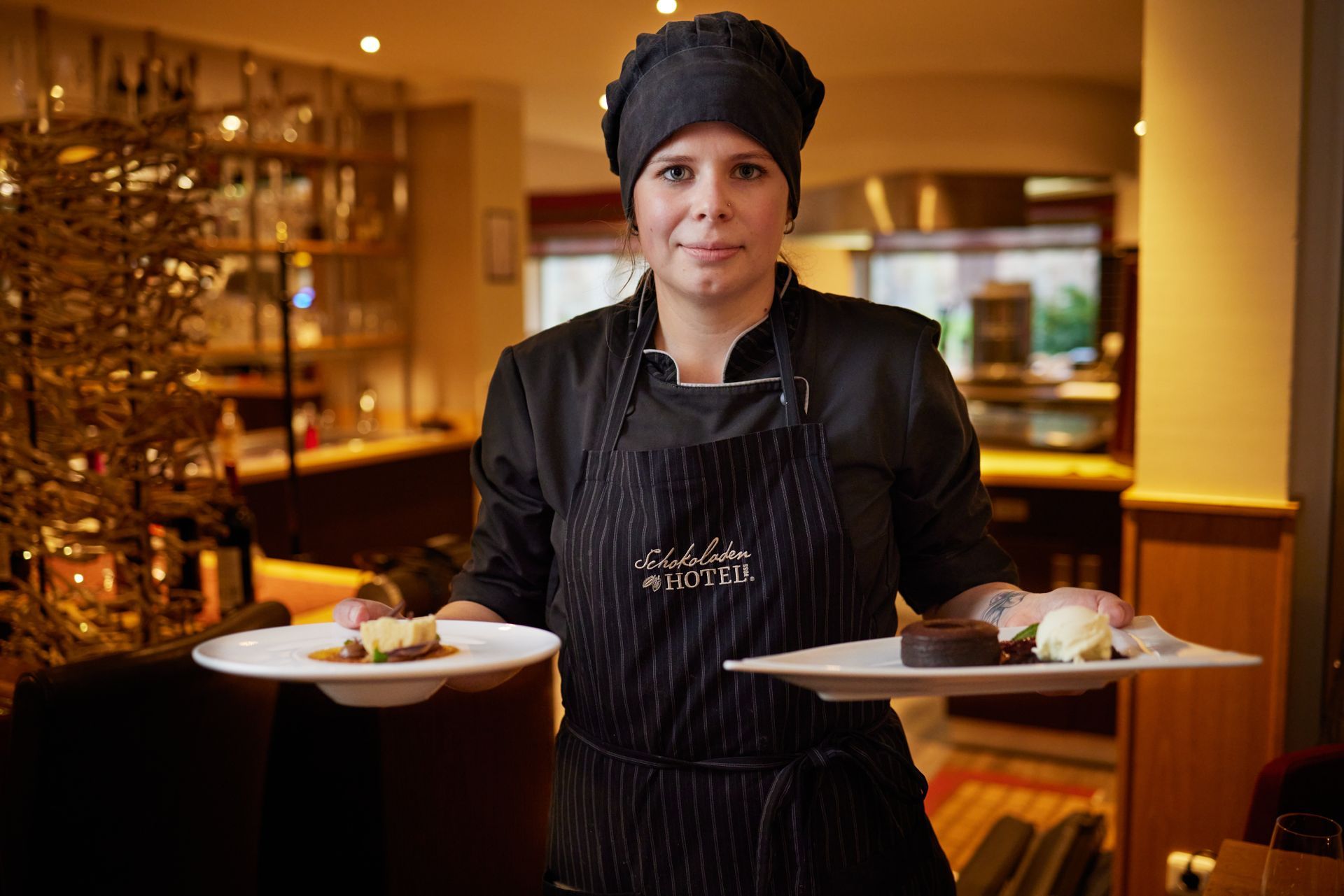 Eine Frau in einer Schürze hält zwei Teller mit Essen.