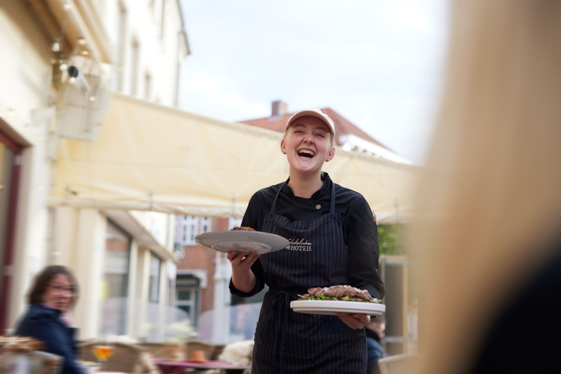 Eine Frau in einer Schürze hält einen Teller mit Essen und lächelt.