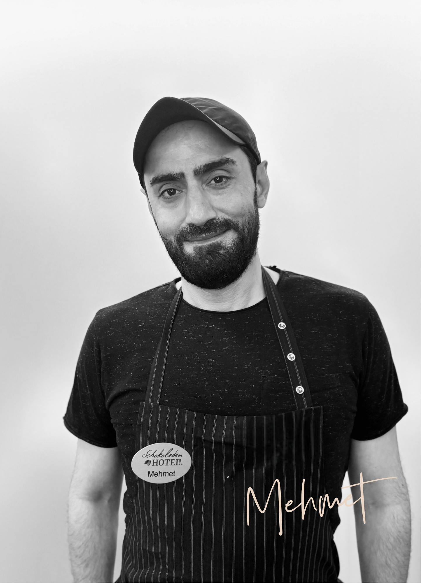 Mann mit schwarzer Schürze und Mütze, lächelnd. Er heißt Mehmet.