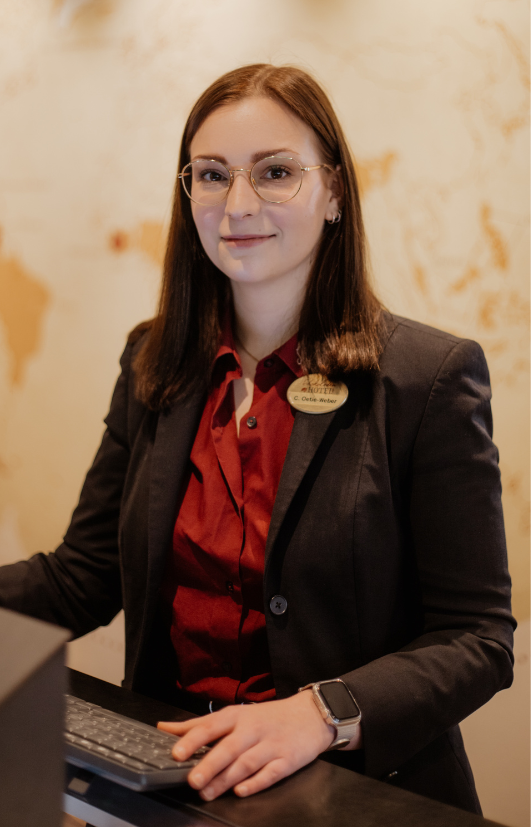 Eine Frau in Anzug und rotem Hemd steht an einem Schreibtisch.