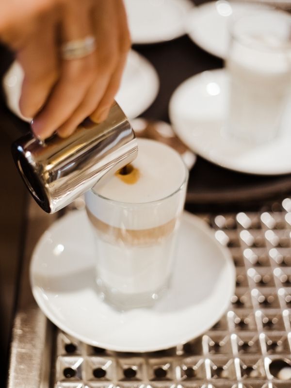Eine Person gießt Kaffee in ein Glas mit Milch gefüllt