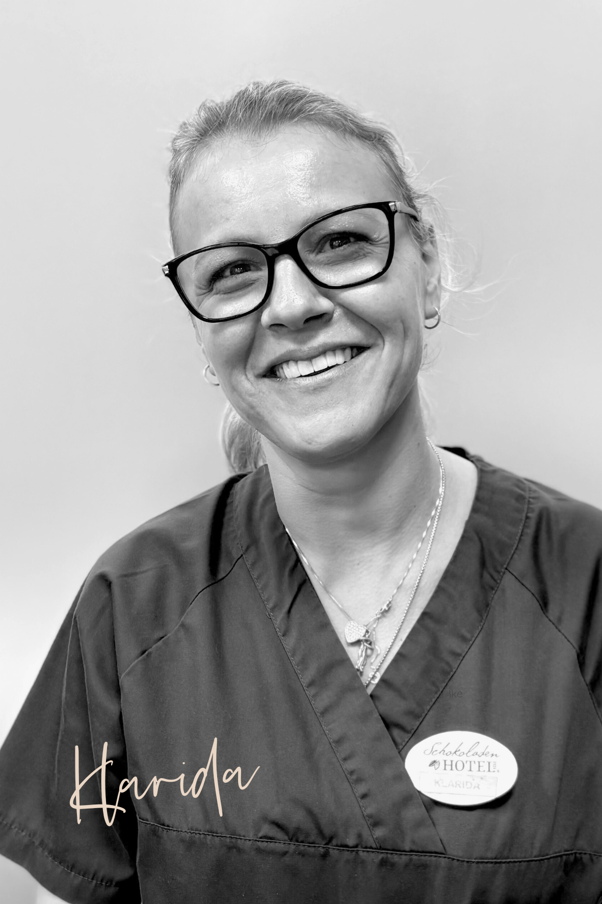 Frau mit Brille, OP-Kleidung und Namensschild lächelt in die Kamera.